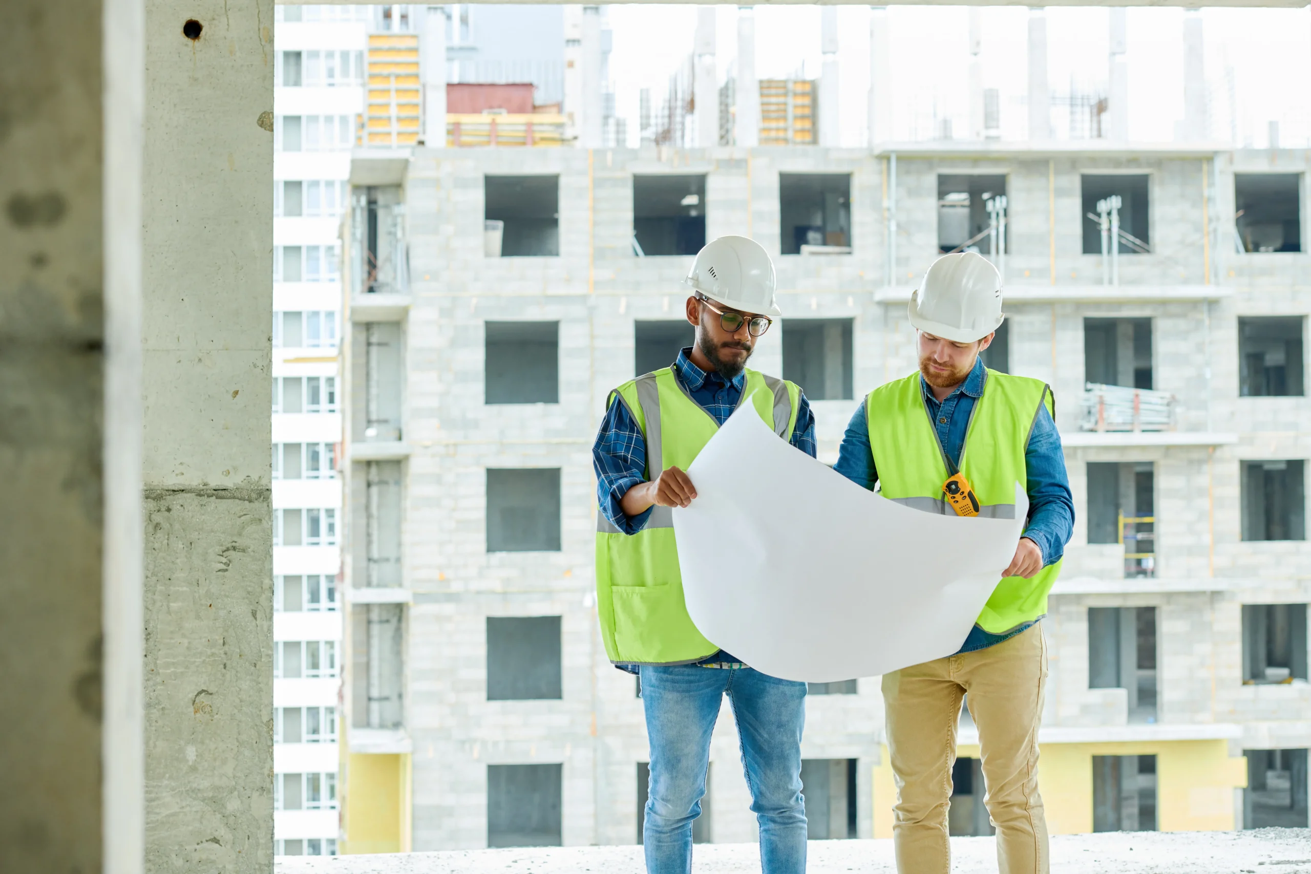 Two construction workers reviewing blueprints at a building site